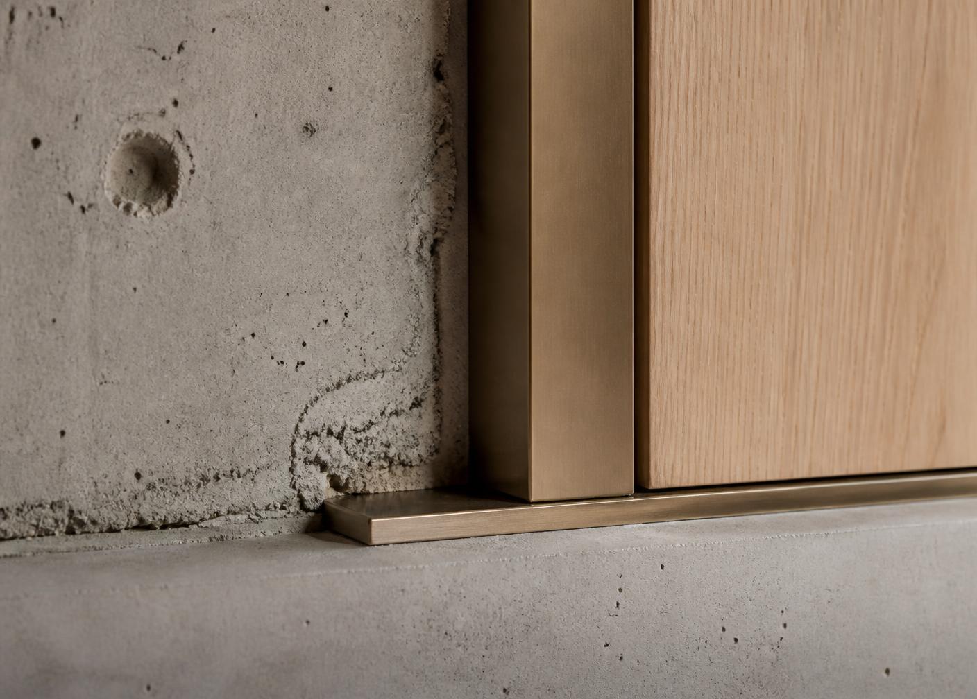 Renovation detail of concrete wall meeting bronze trim and oak panel